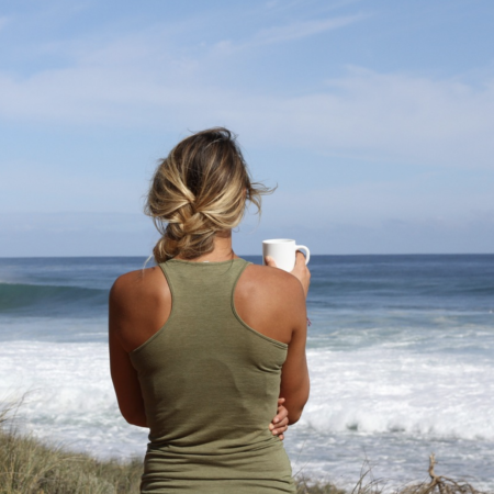 Kvinde ser ud over havet med kop kvadrat